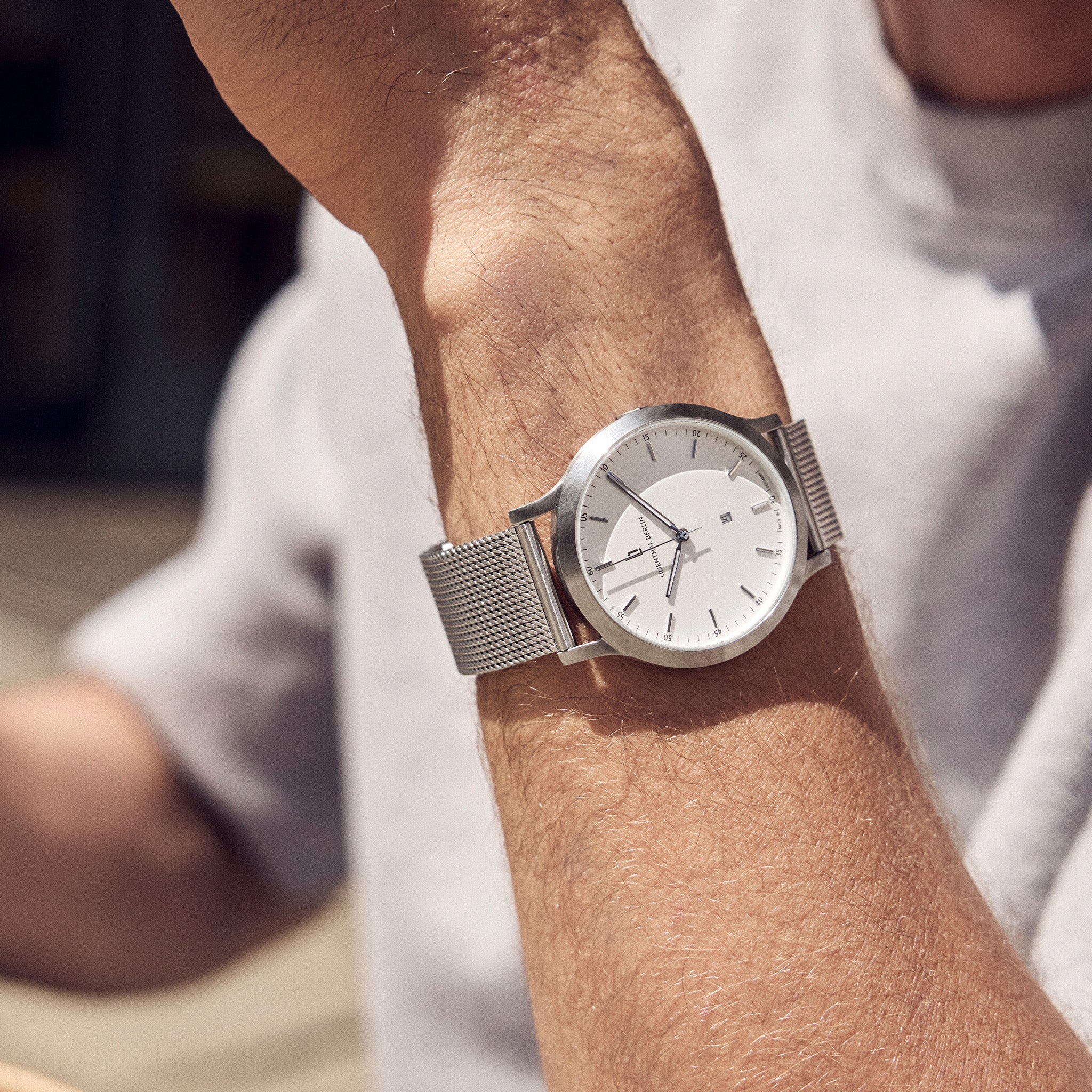 Minimalist silver mesh watch with white dial on wrist, modern and elegant style