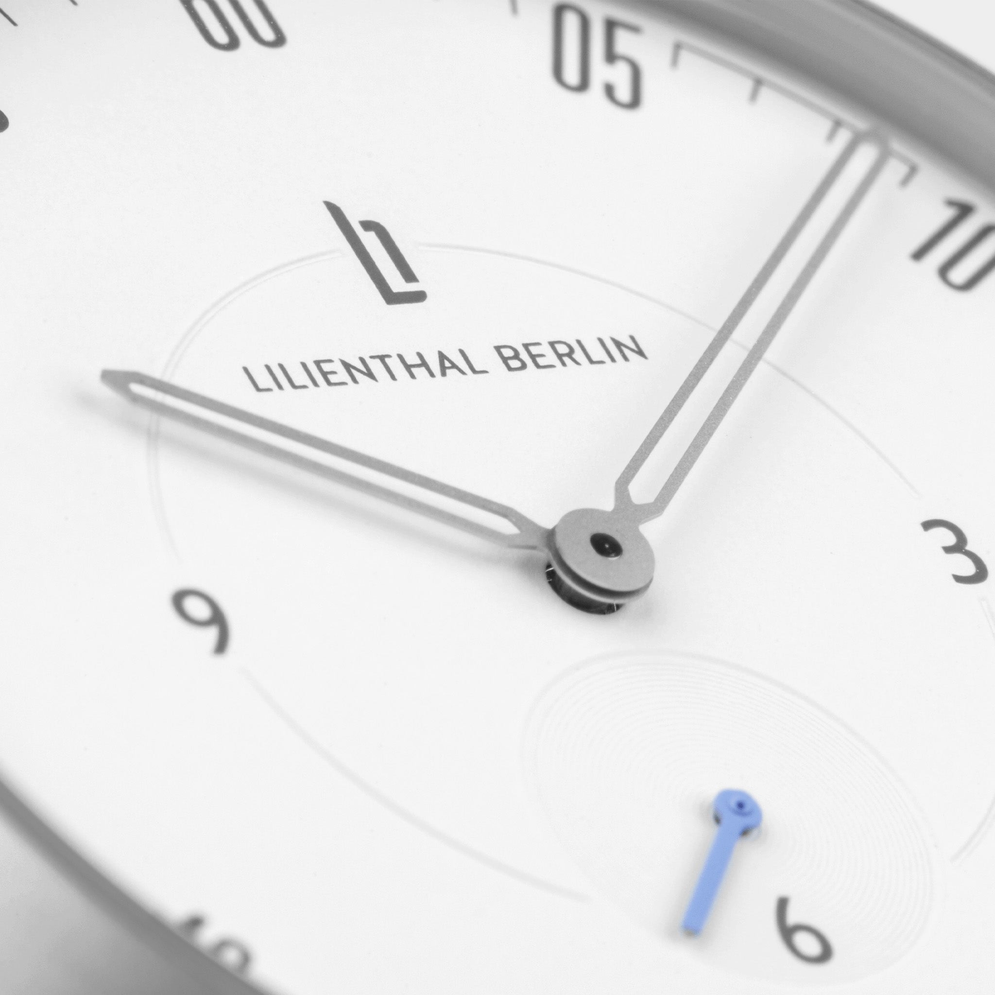 Minimalist white watch face with silver hands and a blue subdial hand
