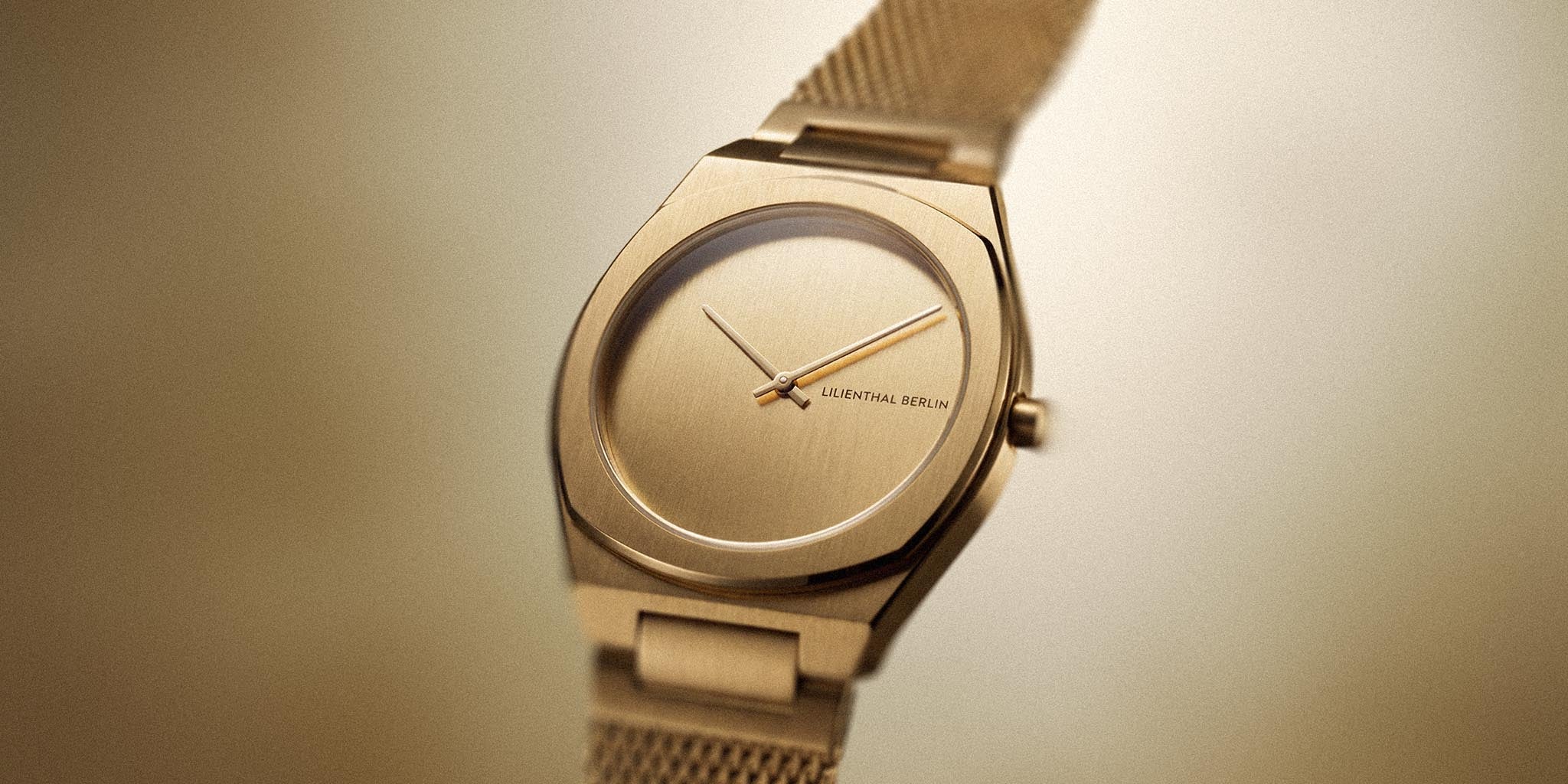 Minimalist gold wristwatch with mesh band and brushed dial on neutral background