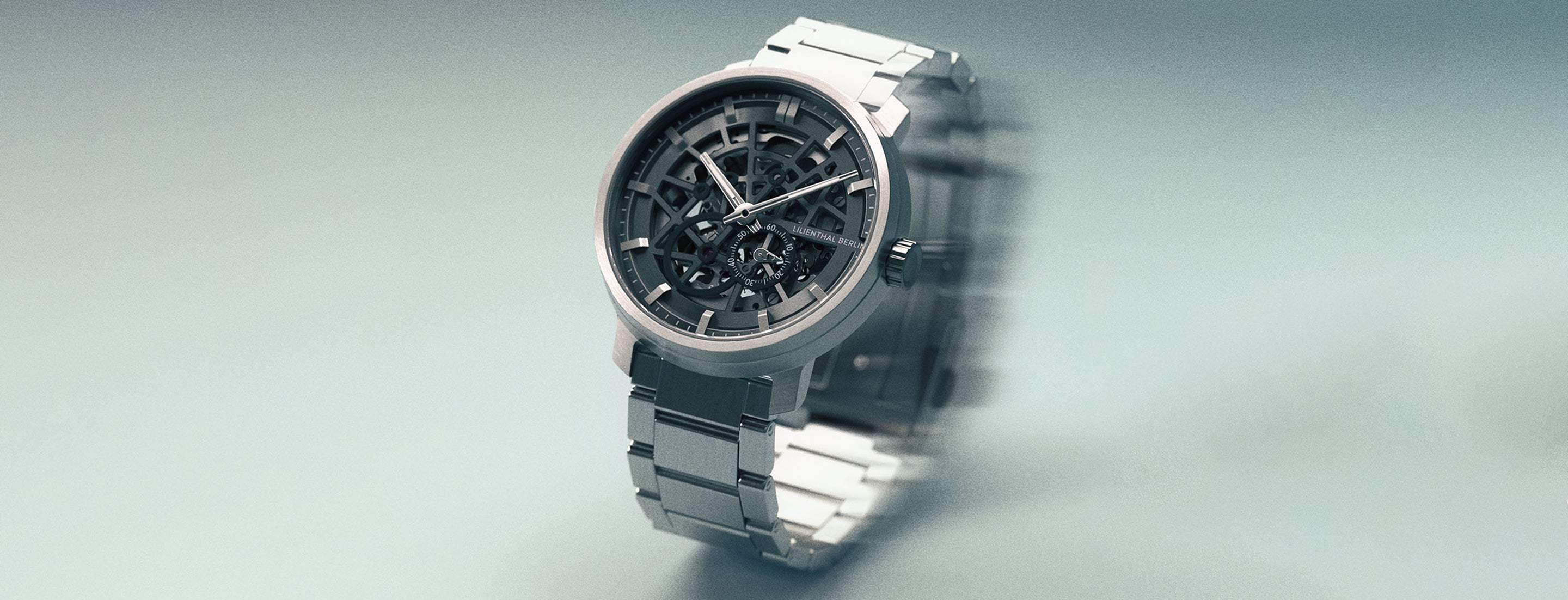 Stainless steel skeleton watch with open dial and metal bracelet on light background