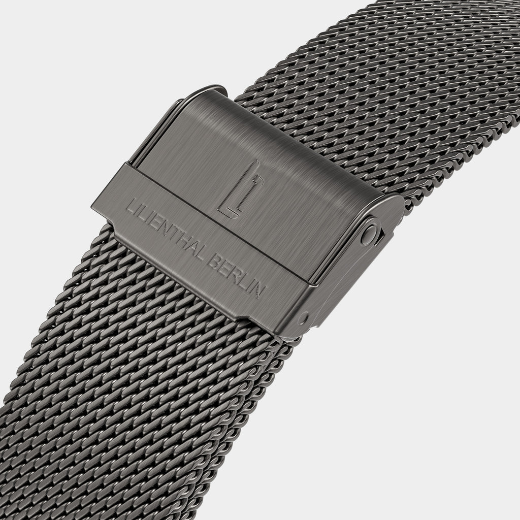 Close-up of a stainless steel mesh watch strap with clasp and engraved branding