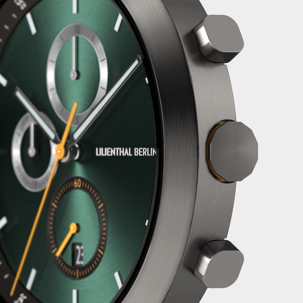 Close-up of a green chronograph watch face with silver dials and orange accents