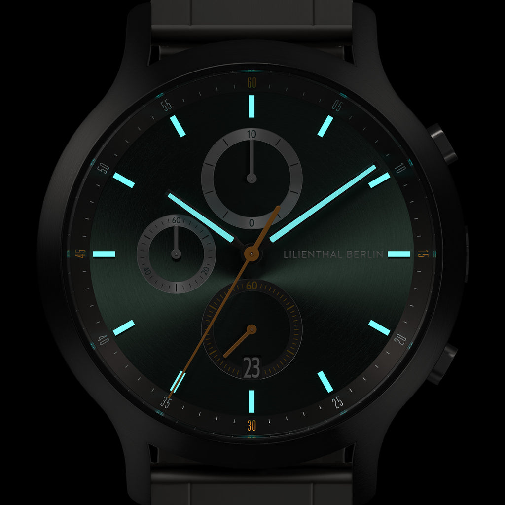 Close-up of modern black chronograph watch face with glowing turquoise markers and subdials.