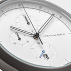 Minimalist white chronograph watch face with subdials, blue hand, and date display