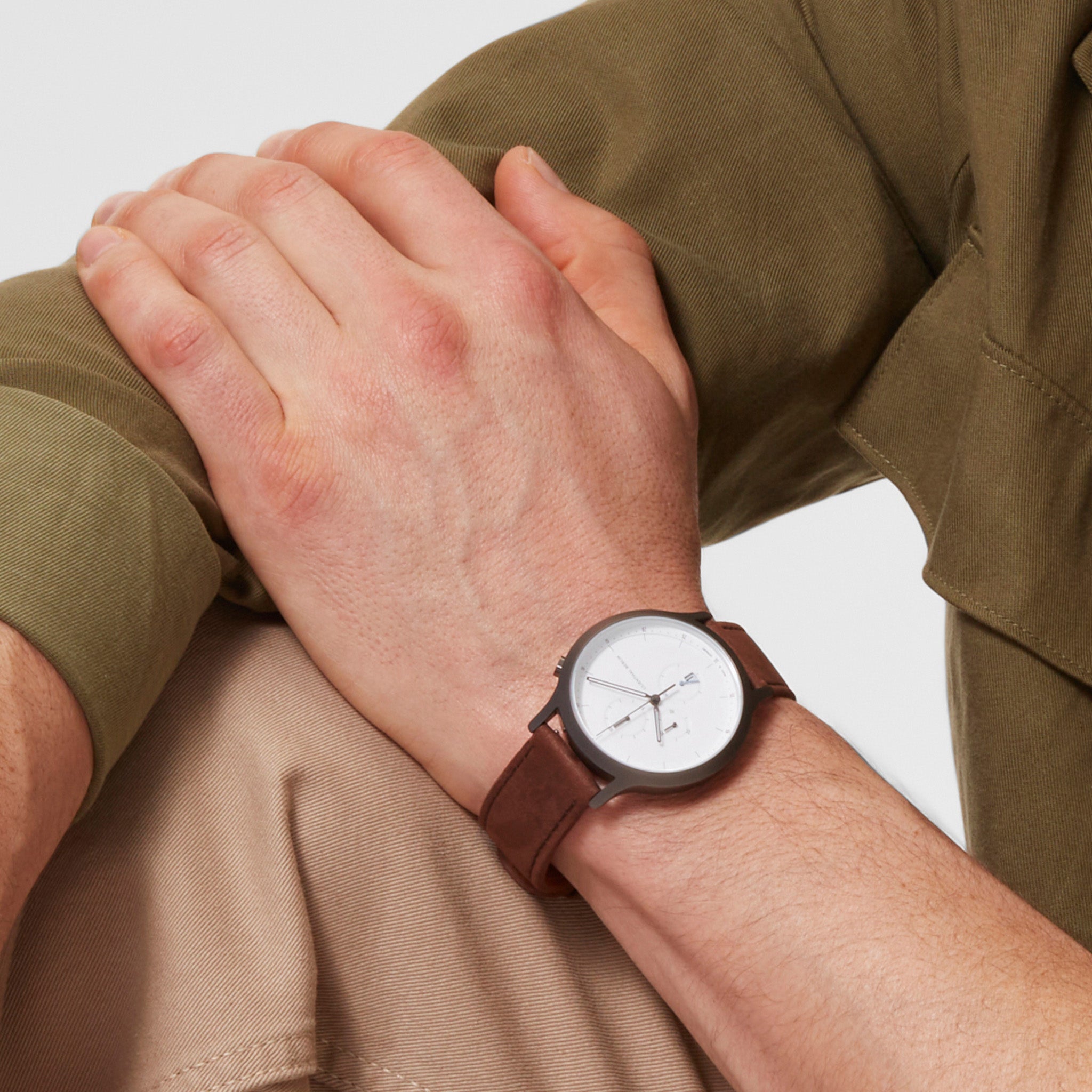 Minimalist wristwatch with white dial and brown leather strap on a person's wrist
