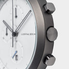 Close-up of a modern chronograph watch with white dial, three subdials, and metal pushers.