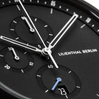 Close-up of a modern black chronograph watch face with subdials, date display, and silver hands.