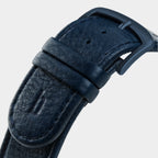 Close-up of a textured dark blue leather watch strap with matte black buckle