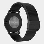 Black stainless steel wristwatch with mesh strap, showing engraved case back and clasp