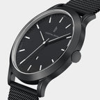 Minimalist black wristwatch with mesh strap and silver hour markers on white background