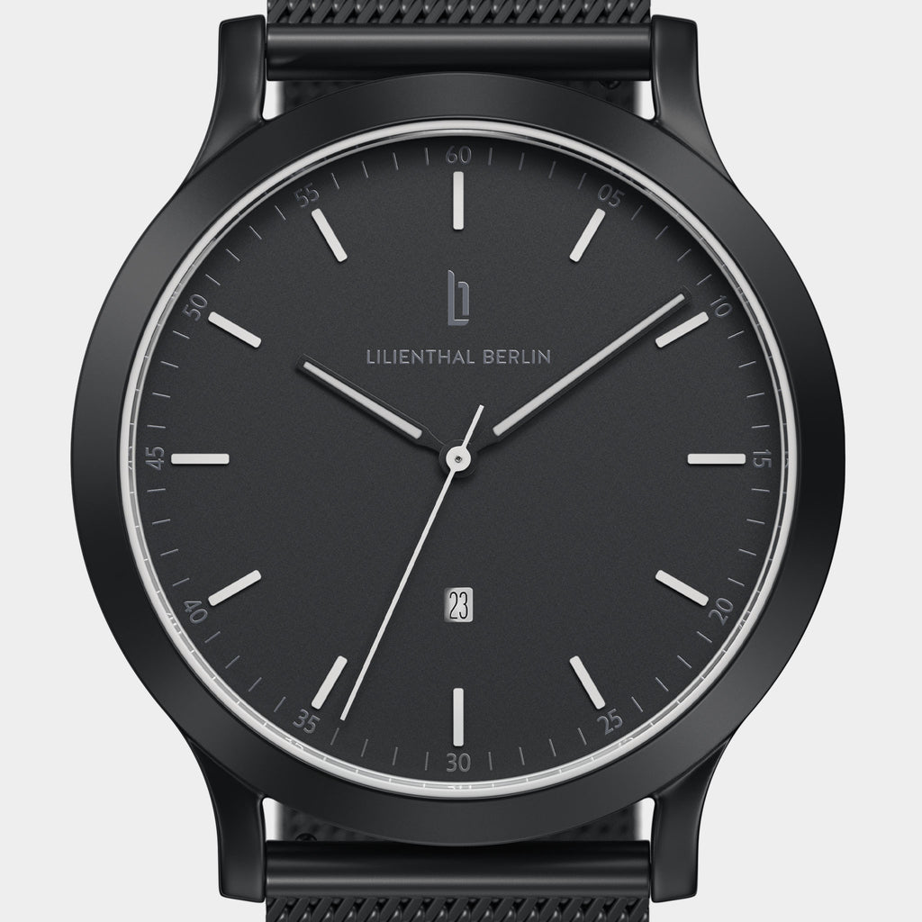 Minimalist black analog watch with date display and mesh strap, close-up on face