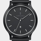 Minimalist black analog watch with date display and mesh strap, close-up on face