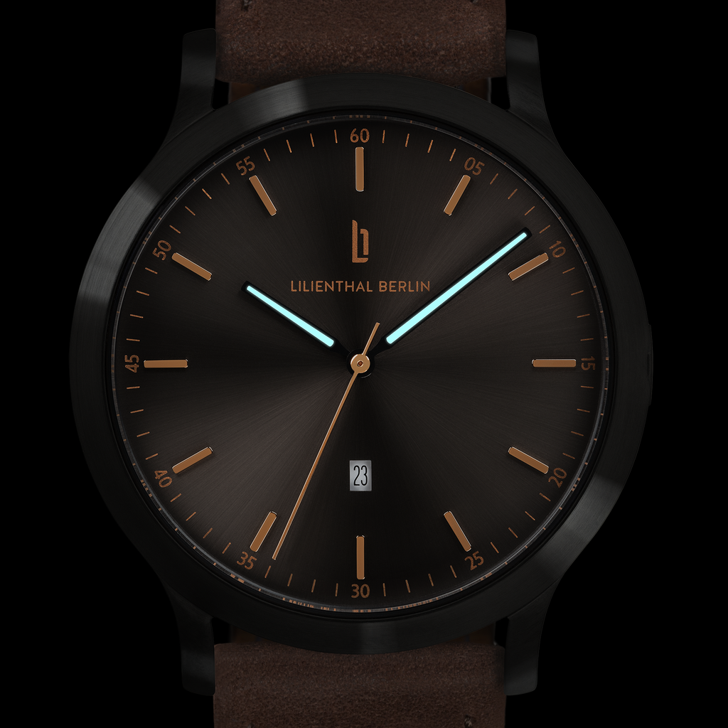 Modern black analog wristwatch with brown strap, gold markers, luminous hands, and date display