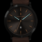 Modern black analog wristwatch with brown strap, gold markers, luminous hands, and date display