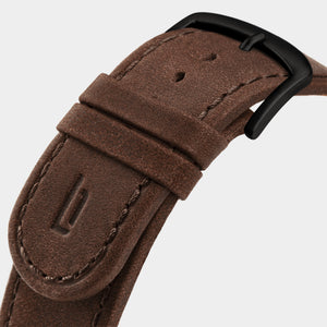 Brown leather watch strap with black buckle and stitched detailing on light background