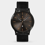 Men's black leather strap watch with dark sunburst dial, gold-tone markers, and date window