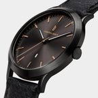 Minimalist black wristwatch with rose gold accents and black leather strap, close-up view