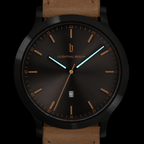 Modern black watch with brown leather strap, minimalist dial, gold accents, and date display