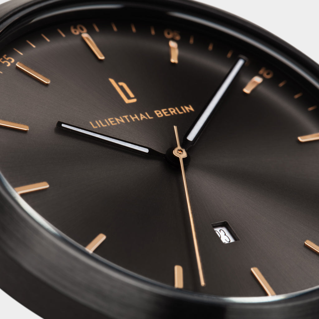 Close-up of a black minimalist watch with gold markers, date display, and sleek hands.