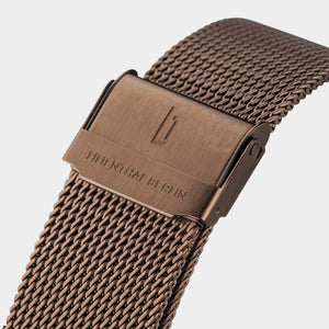 Close-up of bronze mesh watch strap with engraved clasp and modern design.