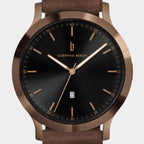 Minimalist wristwatch with black dial, bronze case, brown leather strap, and date display