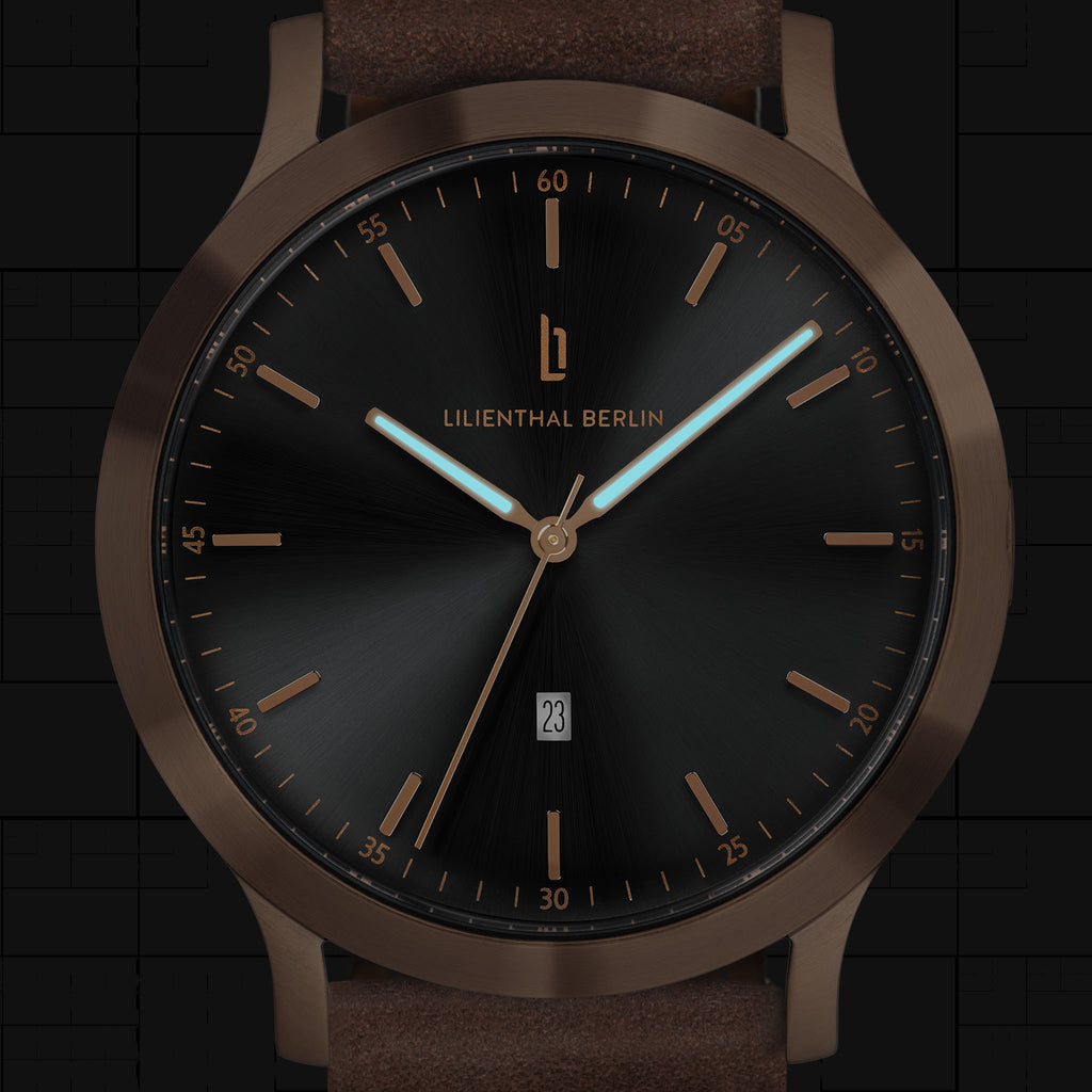 Minimalist black and bronze analog wristwatch with brown leather strap and date display