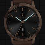 Minimalist black and bronze analog wristwatch with brown leather strap and date display