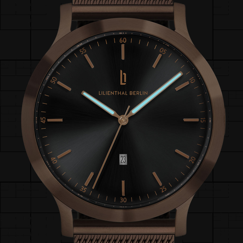 Black and bronze minimalist watch with date display and mesh band, close-up dial view