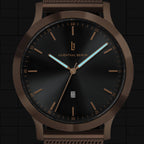 Black and bronze minimalist watch with date display and mesh band, close-up dial view