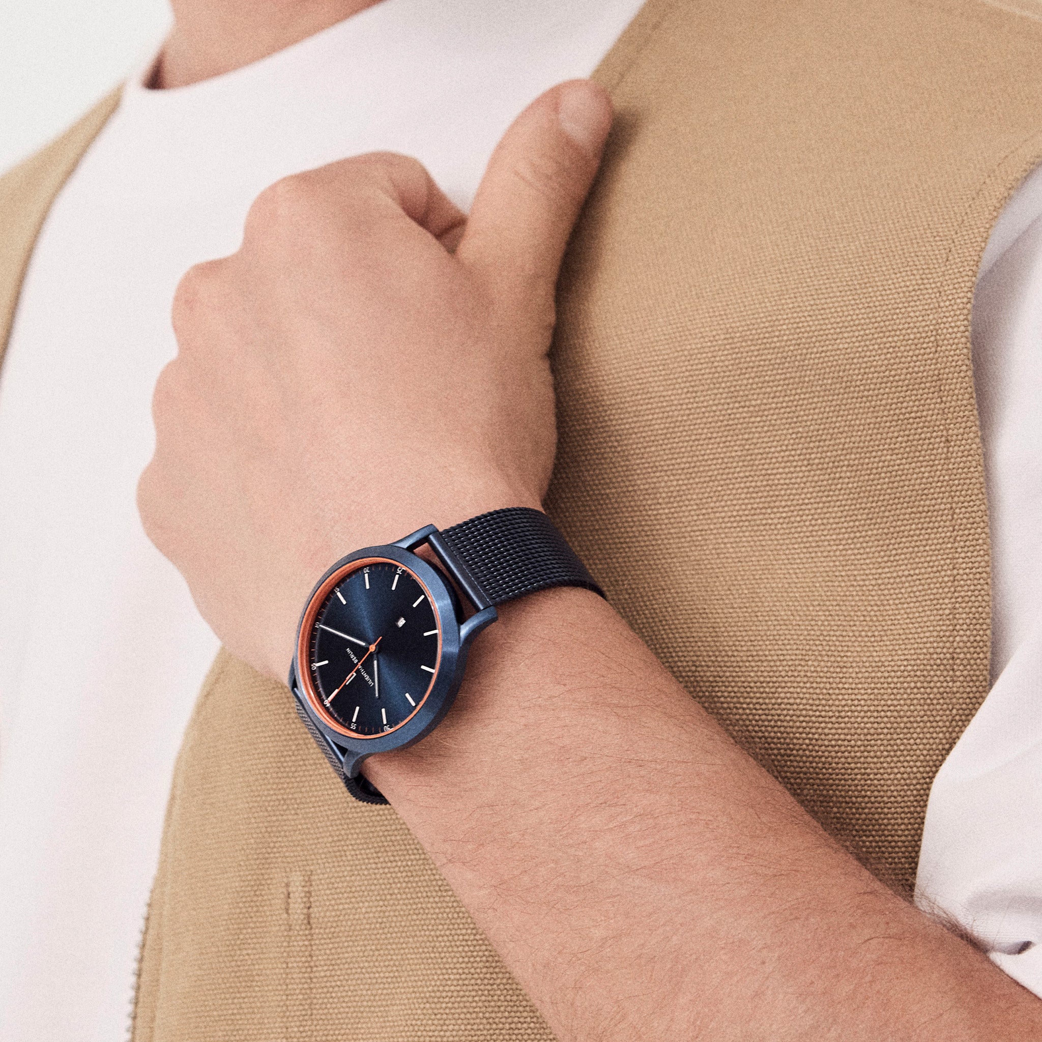 Man wearing minimalist blue wristwatch with mesh strap and copper bezel
