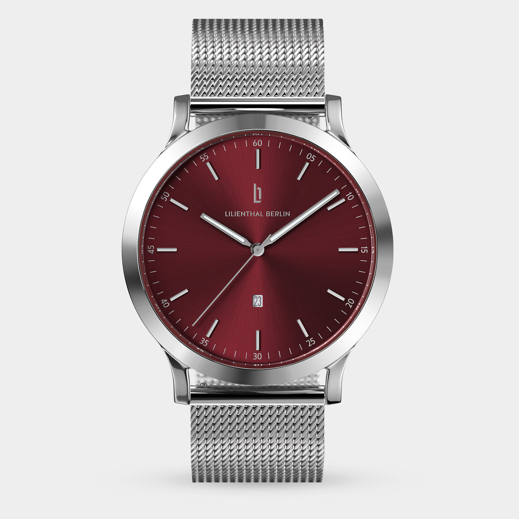 Silver mesh band watch with a red dial and minimalist markers on a neutral background