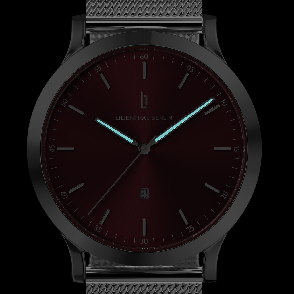 Minimalist wristwatch with black mesh strap, burgundy dial, luminous hands, and date display