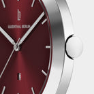 Close-up of a minimalist wristwatch with red dial, silver hands, and stainless steel case
