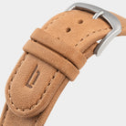 Close-up of tan leather watch strap with metal buckle and embossed decorative emblem