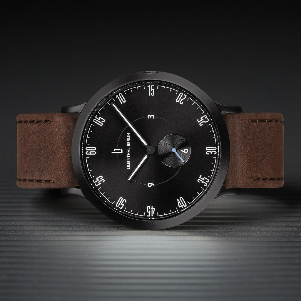 Minimalist black dial watch with brown leather strap on textured surface