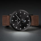 Minimalist black dial watch with brown leather strap on textured surface