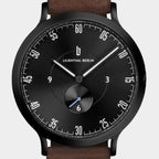 Black minimalist wristwatch with brown leather strap, bold white numerals, and small seconds subdial