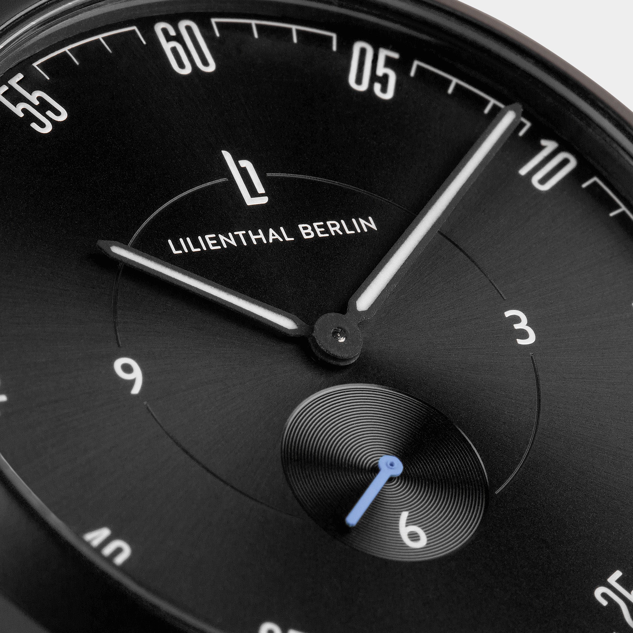 Close-up of a black minimalist watch face with white hands and Lilienthal Berlin logo