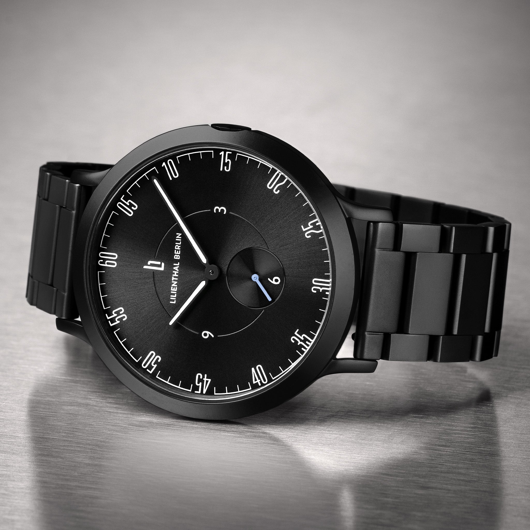 Black minimalist wristwatch with black metal band on a metallic surface