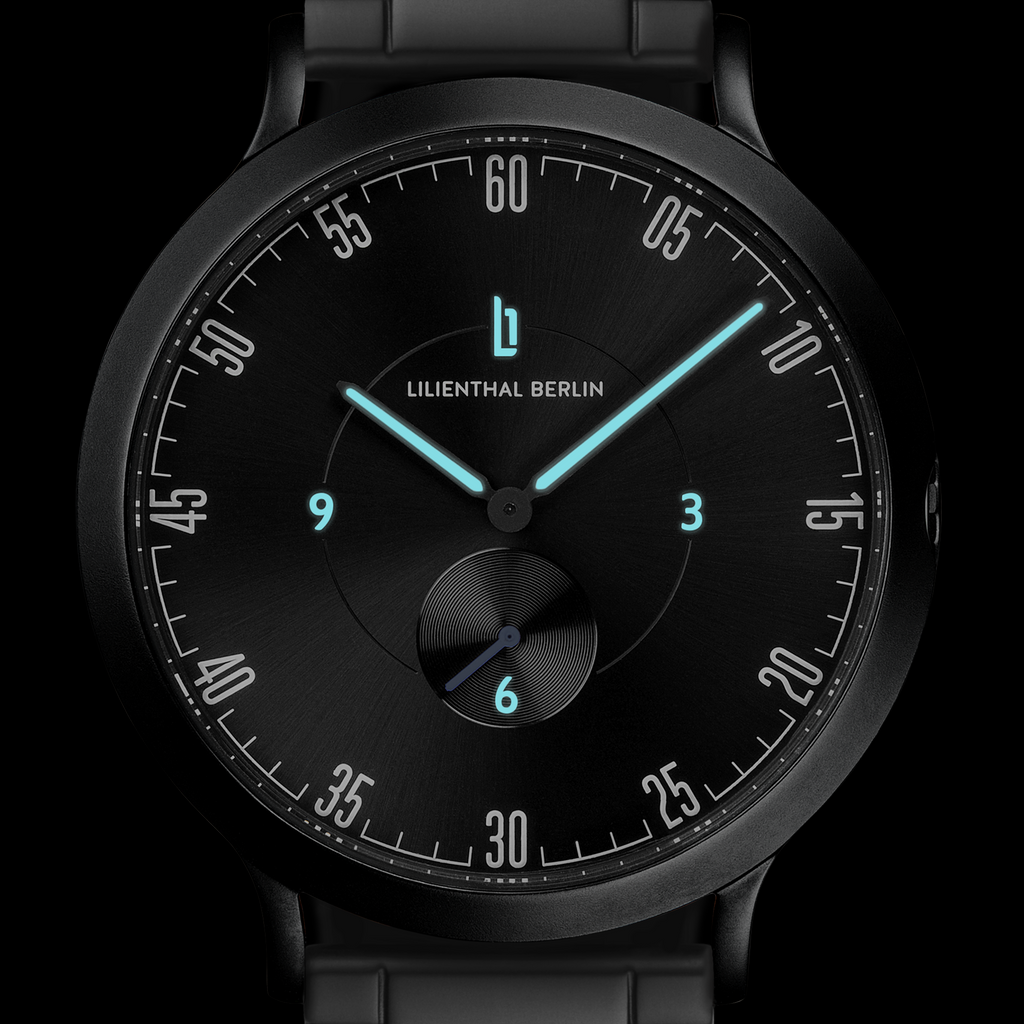 Black minimalist wristwatch with blue luminous hands and subdial on black rubber strap